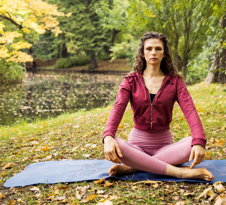 Young sporty female doing yoga exercise outdoor in the park, sport yoga concept. Woman sits on yoga mat.の写真素材
