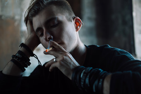 A young blond man smokes a cigarette in a dark room.の写真素材
