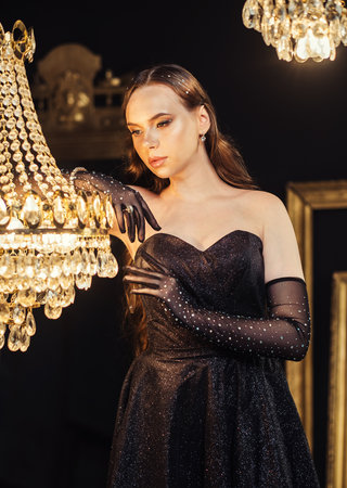 Charming woman in evening dress and gloves in a beautiful room with a luxurious chandelier. Fashion concept.の写真素材