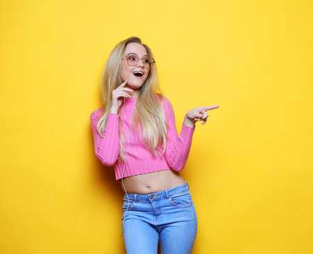 Blonde woman pointing finger, presenting something, portrait on yellow background.の写真素材