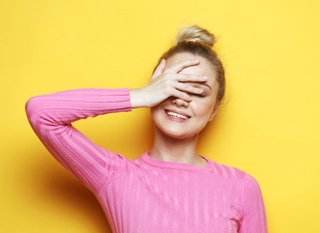 An emotional young woman in a pink jumper smiles and touches her face.の写真素材