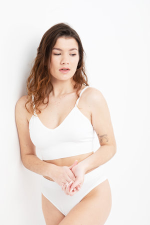 fashion model with long dark curly hair wearing white lingerie posing in studio over white backgroundの写真素材