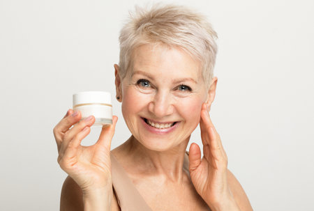 A charming elderly woman with a short hairstyle smiles and holds a jar of cream in her hands.の写真素材