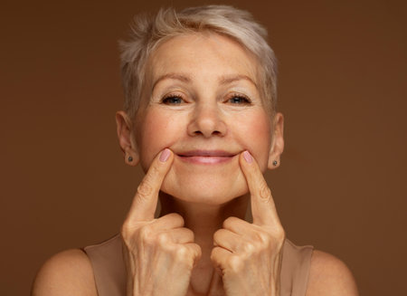Portrait of gorgeous happy mature woman, senior older 60 year lady looking at camera touching her face.の写真素材