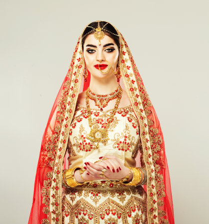 Indian beauty. Young charming woman, dressed in a traditional Indian blouse and covering her head shawl (dupatta). National jewelery set consisting of bright necklace and head adornment (tikka) is decorating her neck and head.の写真素材