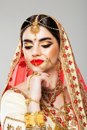 Indian beauty. Gorgeous model wearing in traditional Indian jewelry, with the head covered by veil with gilded edge. Close up.の写真素材