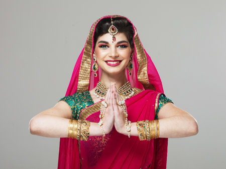 Portrait of beautiful Indian girl dressed in a traditional national suit, showing a gesture of greeting - namaste. Indian young woman dressed in a posh sari costume.の写真素材