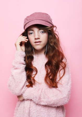 Lifestyle, childhood, emotion and children concept. Girl cute little child wear pink hat and headphones listen music. Pink background.の写真素材