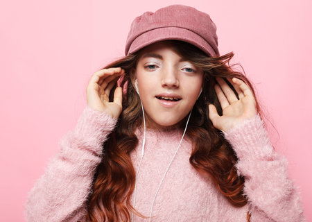 Lifestyle, childhood, emotion and children concept. Girl cute little child wear pink hat and headphones listen music. Pink background.の写真素材