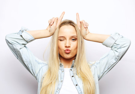 Playful young blond female model shows horns over white backgroundの写真素材