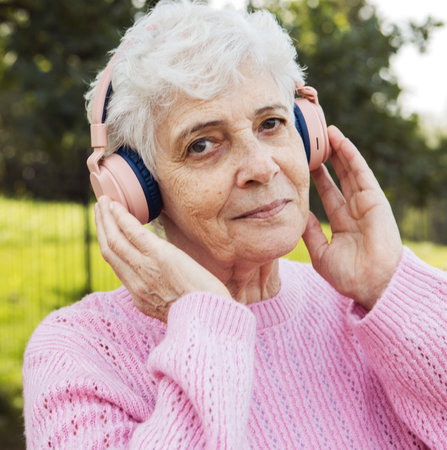 Elderly happy woman in headphones listens to music in the park, concepts about elderly, seniority and wellness agingの写真素材