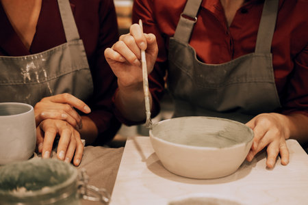 Three cheerful young female friends are painting ceramics in a pottery workshop. Have fun doing art.の写真素材