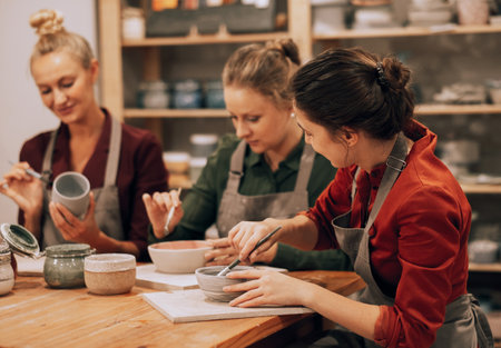 Three cheerful young female friends are painting ceramics in a pottery workshop. Have fun doing art.の写真素材