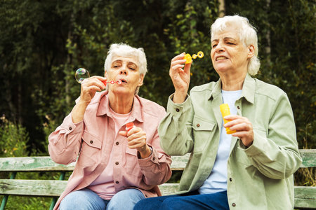 two elderly sisters blowing soap bubbles in a summer park, lifestyle concept.の写真素材