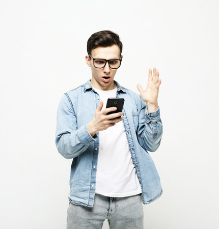 A shocked and dumbfounded man looks at his smartphone reading bad news over white background.の写真素材