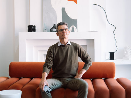 Elderly stylish man sitting on a red sofa in a modern room.の写真素材