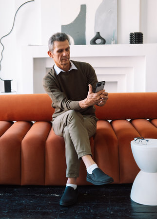 technology, lifestyle and communication concept - senior man dialing phone number and texting on smartphone at homeの写真素材
