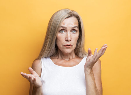 Elderly surprised woman over yellow background, emotional portrait.の写真素材
