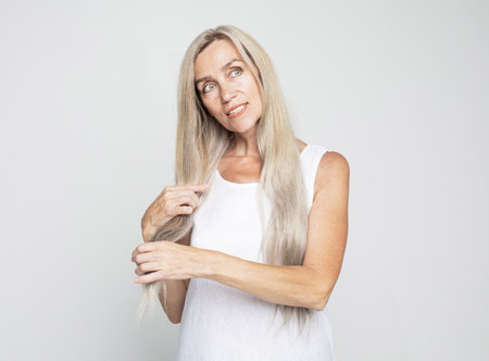 Beauty and old people concept: beautiful senior woman touch long lovely grey hair over light grey background. Close up.の写真素材