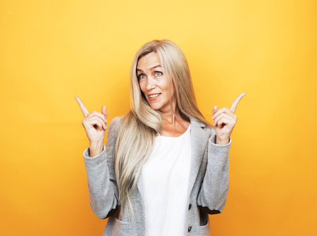 Senior happy woman wearing white t-shirt pointing finger up with successful idea over yellow background.の写真素材