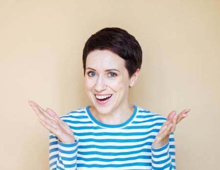 Shocked adult woman in striped shirt, looking at camera over beige background.の写真素材