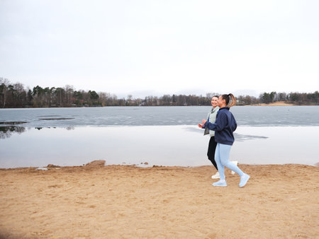 Two sporty female friends are jogging on the beach near a lake on a spring day.の写真素材
