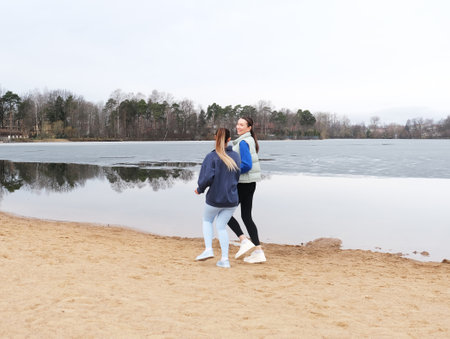 Two sporty female friends are jogging on the beach near a lake on a spring day.の写真素材