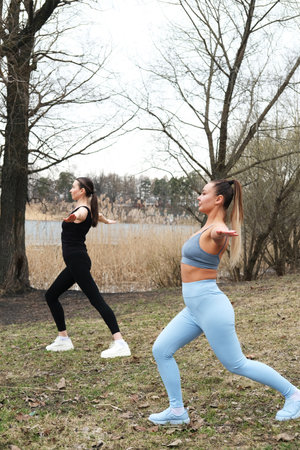 Two women are practicing yoga in a park by a lake, spring day.の写真素材