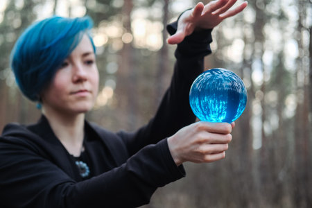 A young woman with blue hair is holding a blue crystal ball in a forest. Scene is mysterious and sereneの写真素材