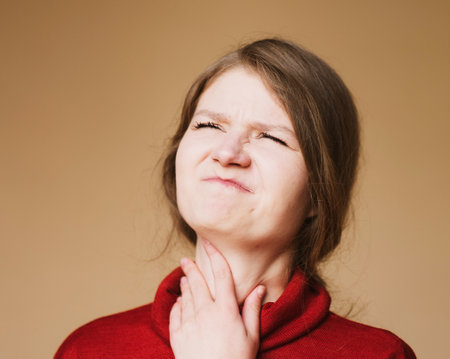 The woman suffers from a sore throat. Portrait over beige background.の写真素材