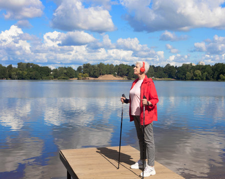 An elderly woman holds walking sticks in her hands and listens to music on headphonesの写真素材