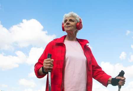 Elderly woman trains endurance while Nordic walking. Old female listening music in headphones.の写真素材