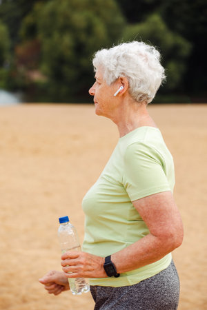 Elderly retired woman jogging. An old woman runs along the beach and holds a bottle of water.の写真素材