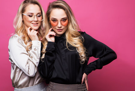 Two beautiful young women in casual clothes posing over pink background.の写真素材