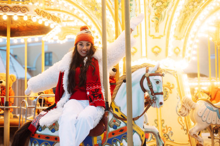Beautiful woman on a carousel. The model is saddled on a horse and having fun during the winter holidays.の写真素材