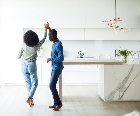 Cheerful millennial black spouses having fun together dancing to music in modern kitchen interior. Happy time.の写真素材