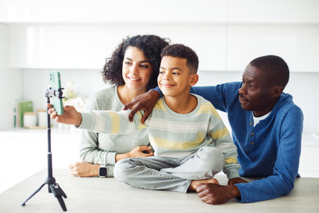 A mixed race family takes a selfie in their modern kitchen using a smartphone with a tripod. Happy time.の写真素材