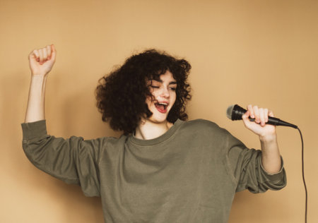 Cheerful young curly-haired young woman sings songs into a microphone and dances.の写真素材