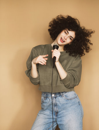 Cheerful young curly-haired young woman sings songs into a microphone and dances.の写真素材