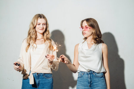 Close-up portrait of two smiling female friends celebrating new year with sparklers. Studio shot of...