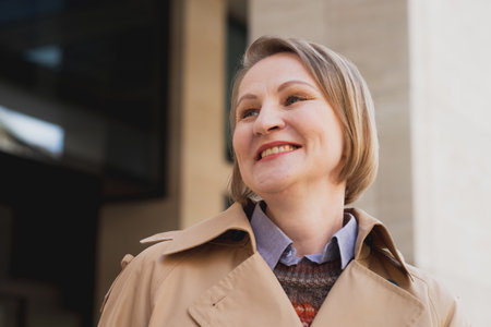Beautiful mature blond woman in beige coat in modern city.