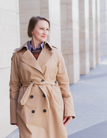 Beautiful mature blond woman in beige coat in modern city.の写真素材
