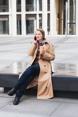 An adult woman talks on the phone and drinks takeaway coffee in a spring city. Lifestyle concept,の写真素材