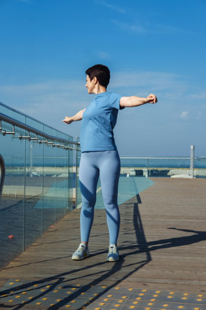 A thirty-year-old sporty woman with a short haircut does morning exercises on a summer day near the ocean.の写真素材