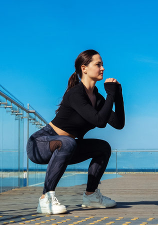 Young sporty woman doing squats outside early in the morning. Leg exercises to maintain good shape.