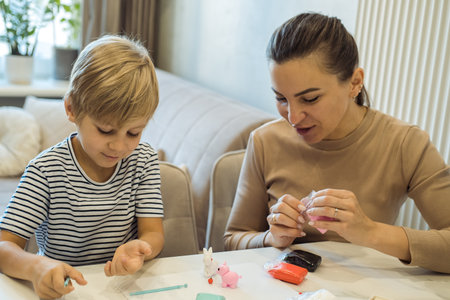 Young mother and her child son moulding together from plasticine figures sitting on table at home....