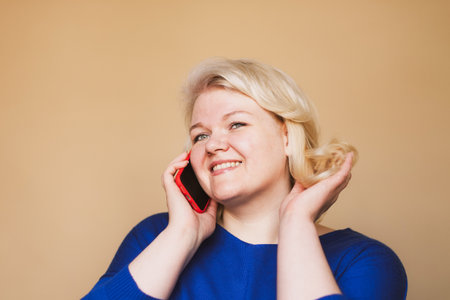 technology, communication and people concept: happy curvy blonde woman with smartphone over beige background.の写真素材