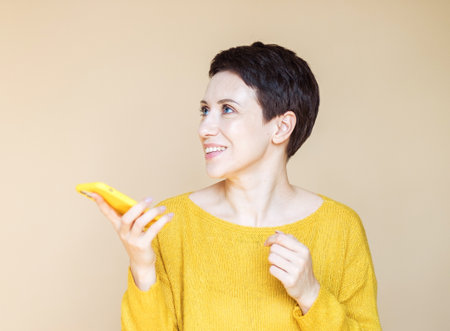 technology, communication and people concept: happy middle age woman with smartphone over beige background.の写真素材