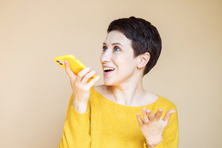 technology, communication and people concept: happy middle age woman with smartphone over beige background.の写真素材
