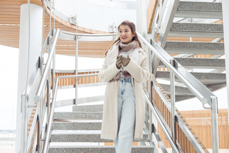 Woman in winter clothes talking on phone in the city. Young woman stay near modern stairs.